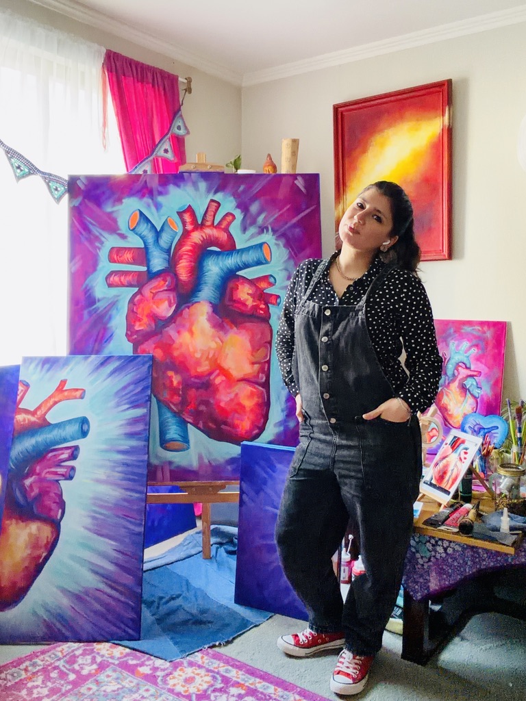 La artista de pie en su taller, junto a varias obras de Hearts & Colors.